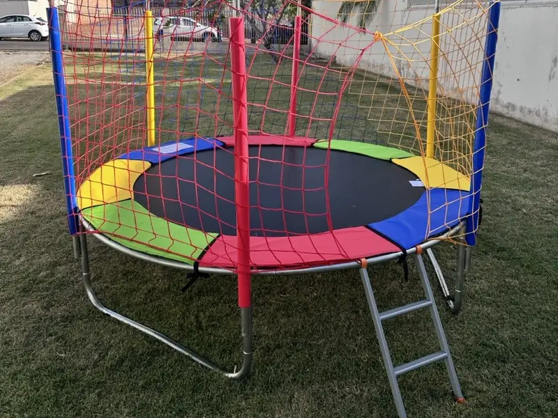Cama elástica com proteção de molas colorida e rede vermelha e amarela, montada sobre a grama