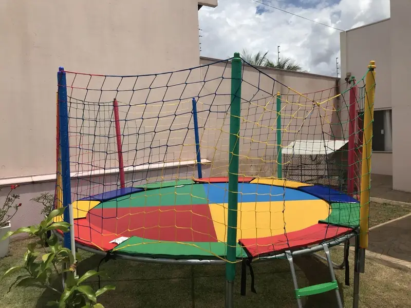 Pula-pula com lona colorida, rede de proteção e escada, montado no gramado de um quintal